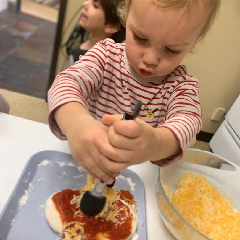 child places cheese on pizza