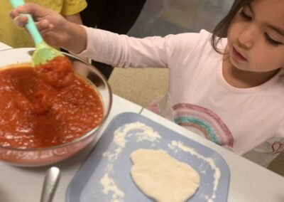 child spoons sauce onto pizza dough